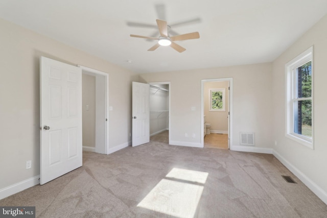 unfurnished bedroom with ceiling fan, light colored carpet, ensuite bathroom, and a spacious closet