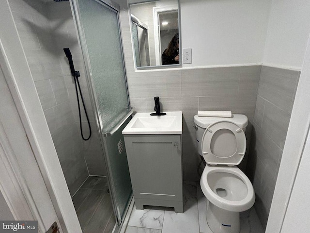 bathroom with vanity, toilet, a shower with door, and tile walls