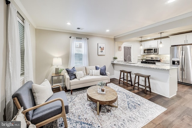 living room featuring hardwood / wood-style floors, crown molding, and sink