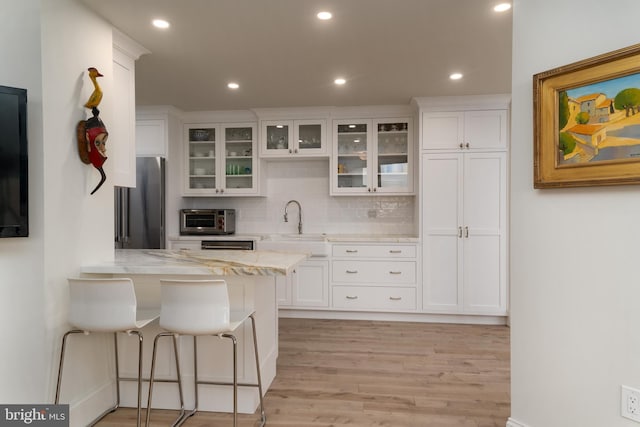 kitchen with white cabinets, sink, stainless steel fridge, light stone counters, and a breakfast bar area