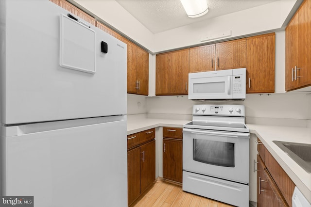 kitchen with sink, white appliances, a textured ceiling, and light wood-type flooring