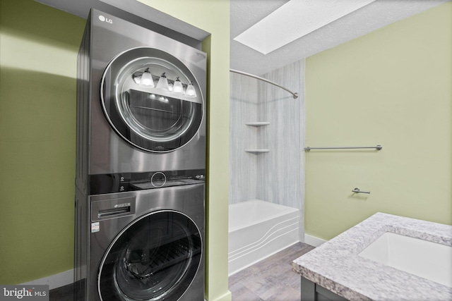 laundry room with hardwood / wood-style flooring, sink, stacked washer and dryer, and a skylight