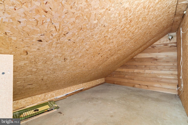 bonus room featuring wood walls, lofted ceiling, and concrete floors