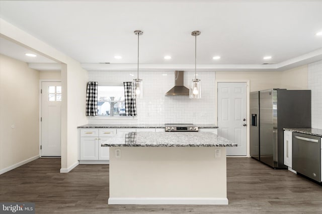 kitchen with light stone countertops, appliances with stainless steel finishes, wall chimney range hood, pendant lighting, and white cabinets