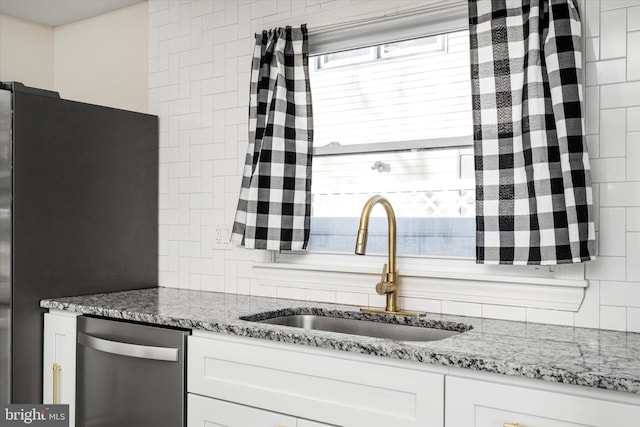 kitchen featuring light stone countertops, white cabinetry, sink, and fridge