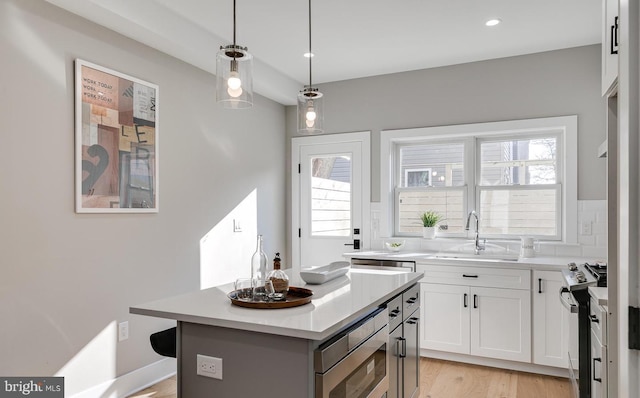 kitchen featuring stainless steel appliances, sink, pendant lighting, a center island, and white cabinetry