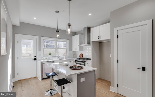 kitchen featuring wall chimney exhaust hood, stainless steel appliances, white cabinetry, a kitchen island, and hanging light fixtures