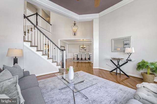 living room featuring wood-type flooring, ceiling fan with notable chandelier, and crown molding