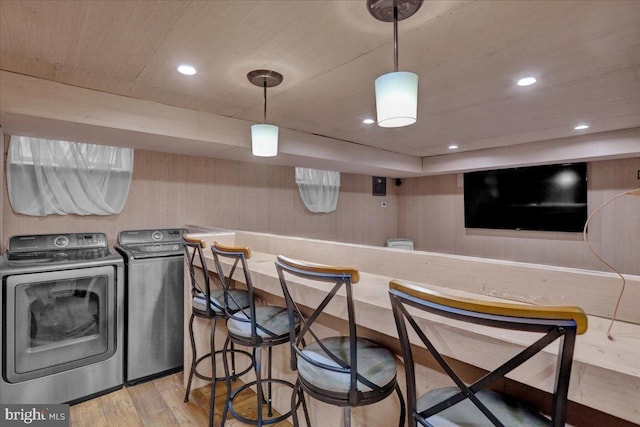 interior space featuring indoor bar, washing machine and clothes dryer, wood walls, and light wood-type flooring