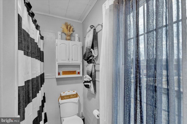 bathroom featuring ornamental molding, toilet, and tile walls