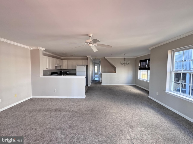 unfurnished living room featuring dark colored carpet, ceiling fan with notable chandelier, and crown molding