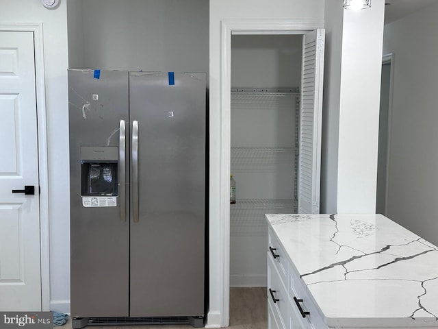 kitchen with light stone counters, white cabinetry, and stainless steel refrigerator with ice dispenser