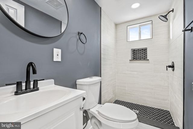 bathroom with tiled shower, vanity, and toilet