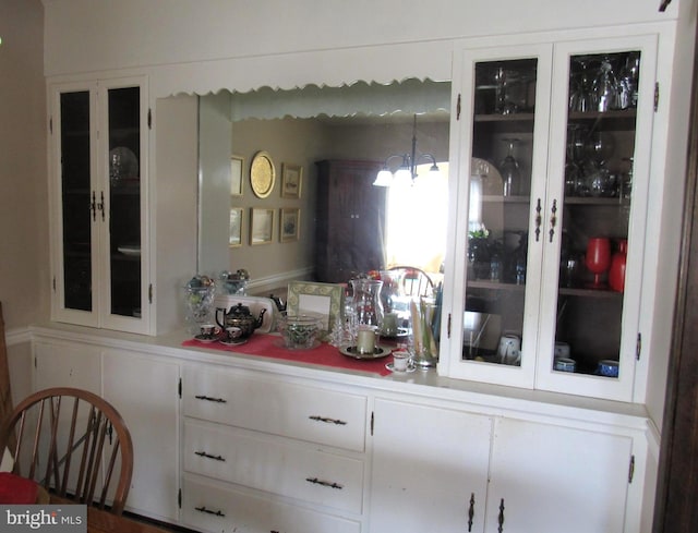 bar with white cabinetry, hanging light fixtures, and a chandelier