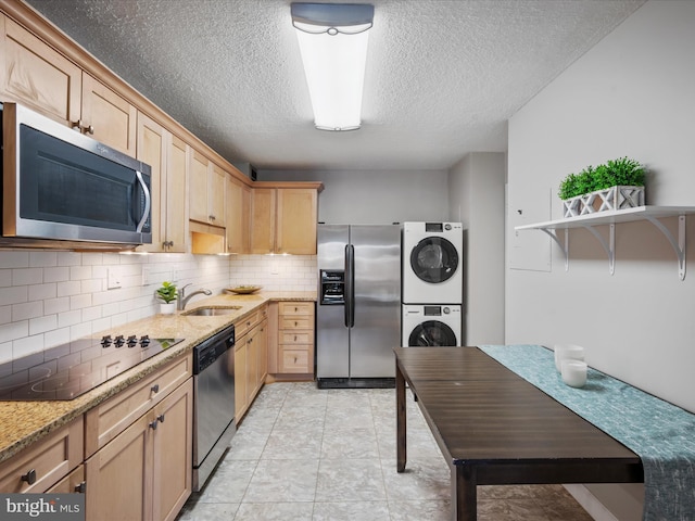 kitchen with light stone counters, stacked washing maching and dryer, sink, stainless steel appliances, and light brown cabinets