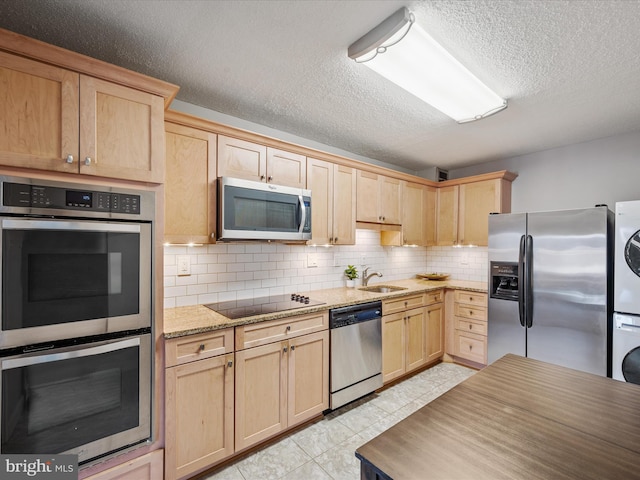 kitchen featuring sink, decorative backsplash, light stone countertops, stacked washer and dryer, and appliances with stainless steel finishes