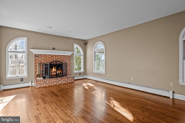 unfurnished living room with baseboard heating, a wealth of natural light, and a brick fireplace