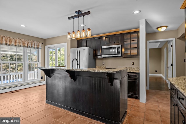 kitchen featuring baseboard heating, a kitchen island with sink, appliances with stainless steel finishes, and a breakfast bar area