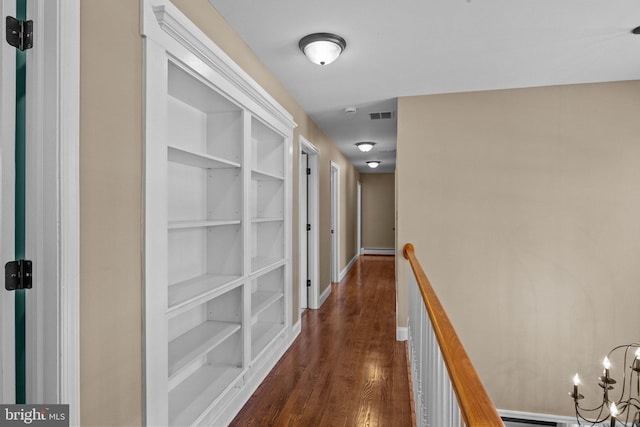 hallway with built in shelves, dark hardwood / wood-style flooring, a baseboard radiator, and a notable chandelier