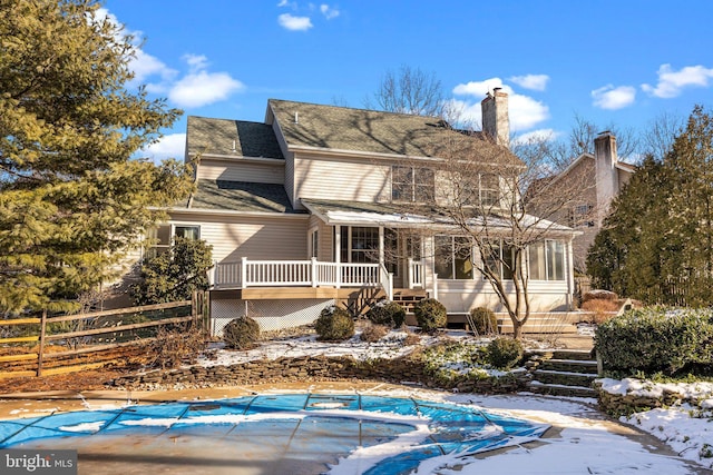 snow covered rear of property featuring a covered pool and a sunroom