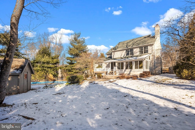 snow covered back of property featuring a storage unit and a sunroom