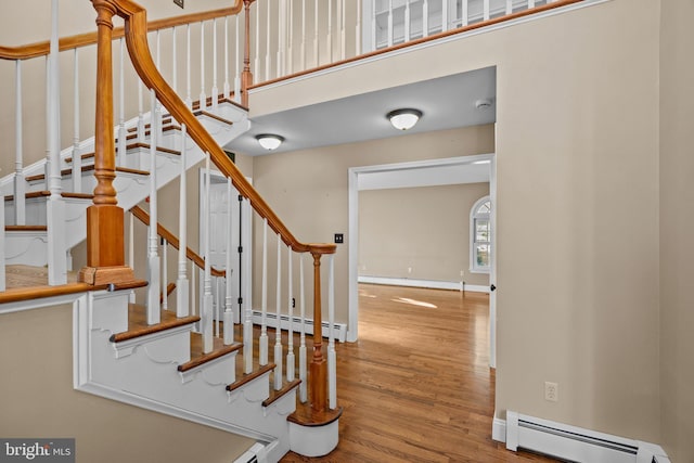 stairway with hardwood / wood-style flooring, a high ceiling, and a baseboard radiator