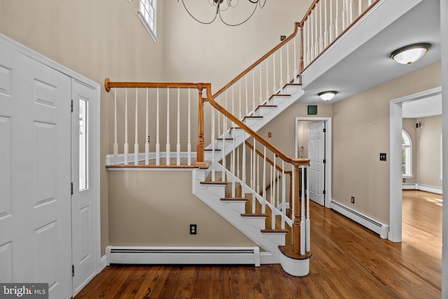 stairway with a chandelier, wood-type flooring, and baseboard heating