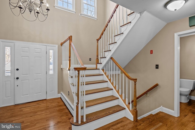 foyer entrance with a towering ceiling, a chandelier, a baseboard radiator, and hardwood / wood-style flooring