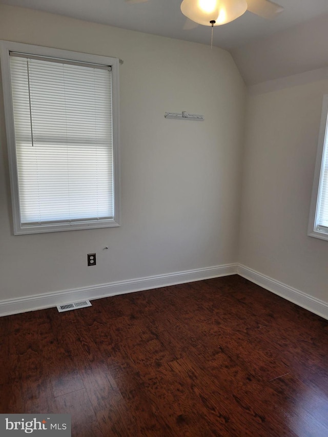 empty room featuring dark wood-style floors, visible vents, vaulted ceiling, ceiling fan, and baseboards