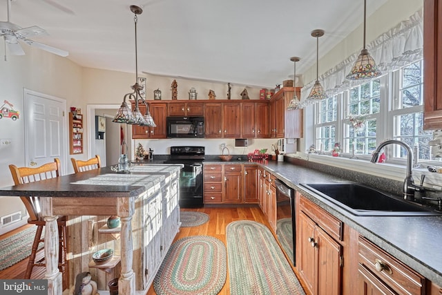 kitchen with pendant lighting, black appliances, sink, ceiling fan, and a breakfast bar area