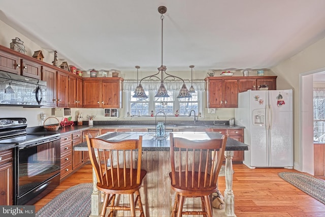 kitchen with white refrigerator with ice dispenser, a kitchen breakfast bar, hanging light fixtures, black / electric stove, and a kitchen island