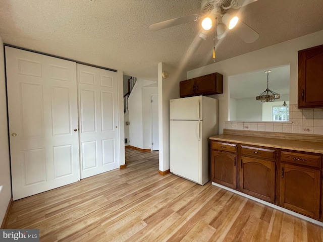 kitchen with light wood-type flooring, tasteful backsplash, ceiling fan, white refrigerator, and decorative light fixtures