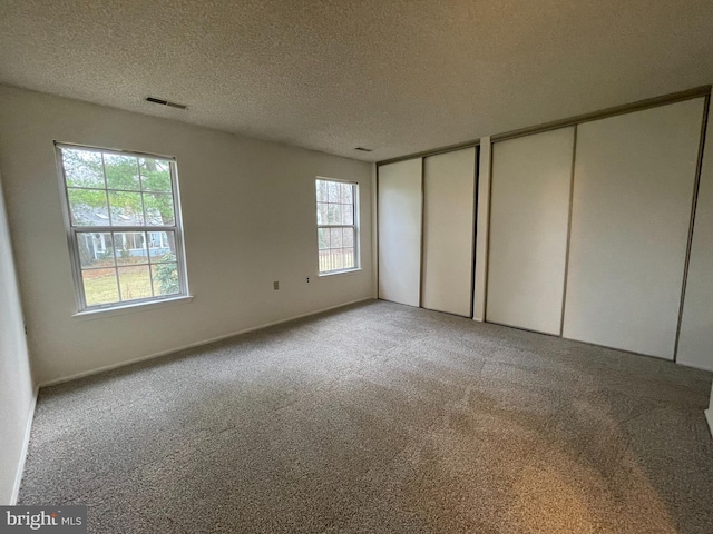 unfurnished bedroom featuring a textured ceiling, two closets, multiple windows, and light colored carpet