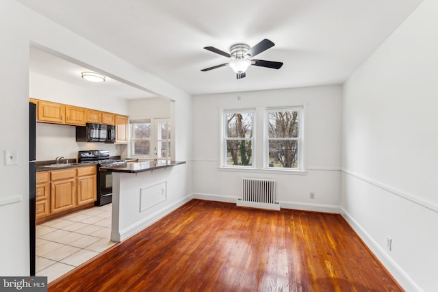 kitchen featuring ceiling fan, radiator heating unit, kitchen peninsula, black appliances, and light wood-type flooring