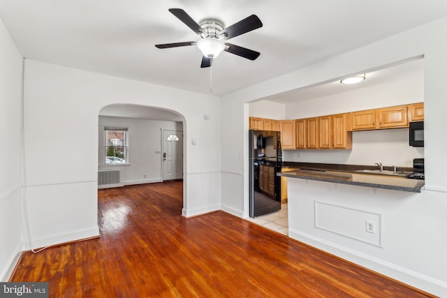 kitchen with black appliances, sink, ceiling fan, light hardwood / wood-style floors, and radiator heating unit