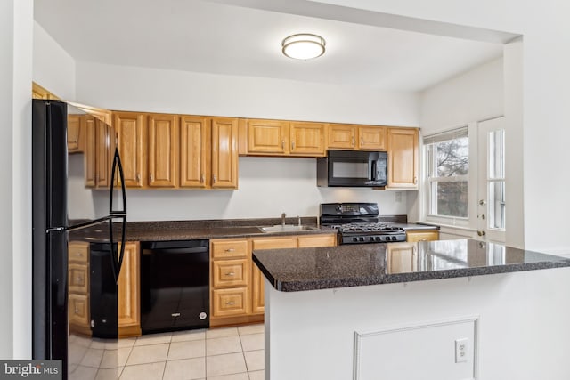 kitchen featuring dark stone countertops, sink, light tile patterned floors, and black appliances