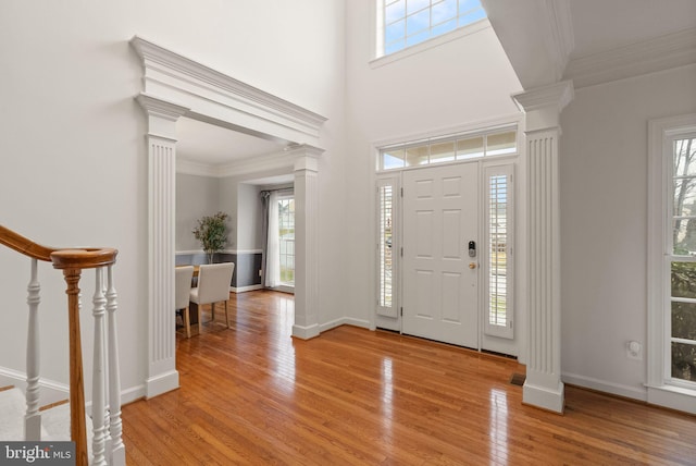 entrance foyer with ornate columns, ornamental molding, a towering ceiling, and hardwood / wood-style floors