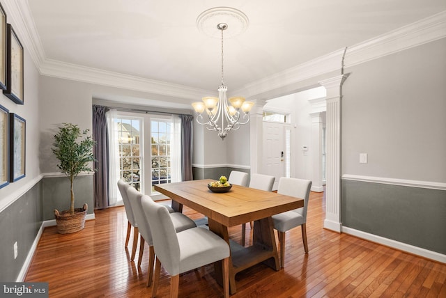 dining area featuring crown molding, hardwood / wood-style flooring, decorative columns, and an inviting chandelier