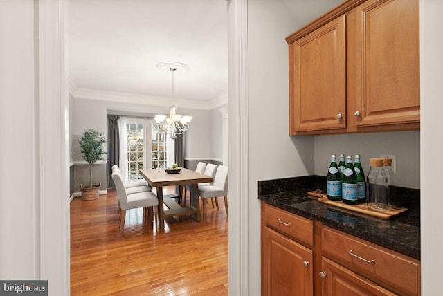 kitchen featuring crown molding, an inviting chandelier, decorative light fixtures, dark stone countertops, and light hardwood / wood-style floors