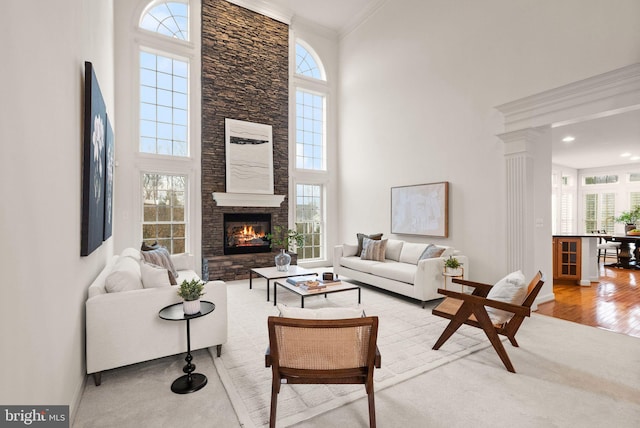 living room featuring a towering ceiling, a fireplace, decorative columns, ornamental molding, and light hardwood / wood-style floors