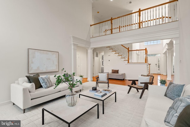 living room with decorative columns, a towering ceiling, and light wood-type flooring