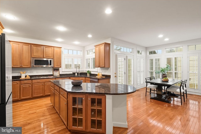 kitchen with sink, appliances with stainless steel finishes, dark stone countertops, a kitchen island, and light wood-type flooring