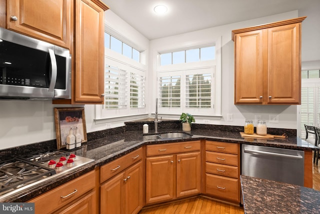 kitchen with appliances with stainless steel finishes, sink, dark stone counters, and light wood-type flooring