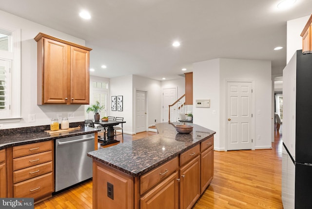 kitchen featuring a kitchen island, stainless steel dishwasher, dark stone counters, and light wood-type flooring