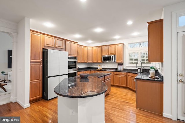 kitchen with sink, appliances with stainless steel finishes, light hardwood / wood-style floors, a kitchen island, and dark stone counters