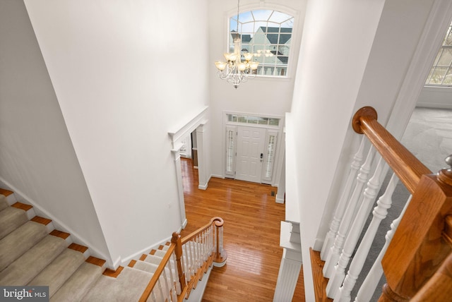 stairs with hardwood / wood-style flooring, a towering ceiling, and a notable chandelier