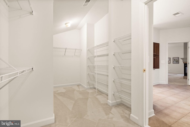 walk in closet with light colored carpet and a multi sided fireplace