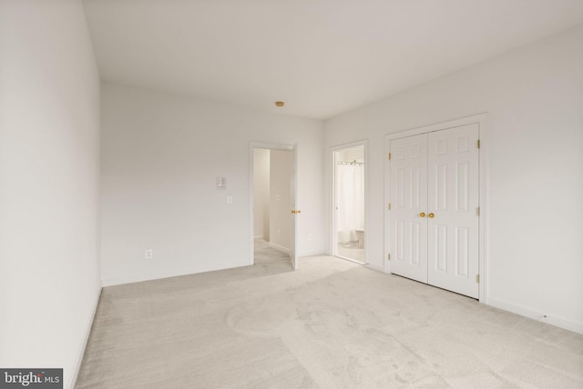 unfurnished bedroom featuring light colored carpet, a closet, and ensuite bath