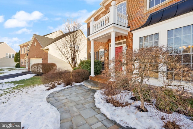 snow covered property entrance with a garage and a balcony