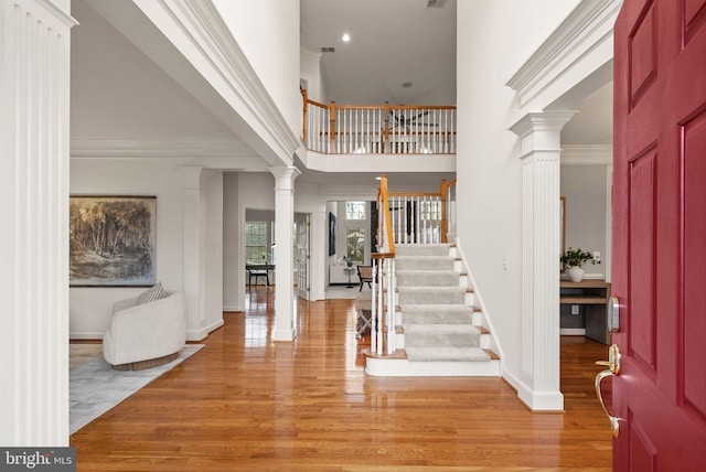 foyer entrance featuring ornate columns, crown molding, a towering ceiling, and light hardwood / wood-style flooring